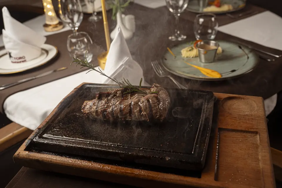 Un steak servi sur une pierre chaude posée sur une planche en bois
