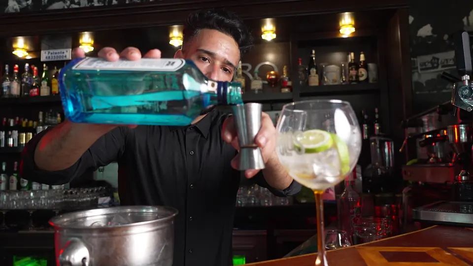 Le barman verse du gin dans un grand verre garni de citron vert