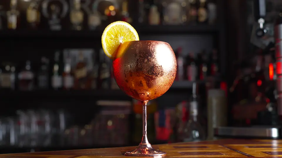 Un verre à gin cuivré garni d’une tranche d’orange, sur le comptoir