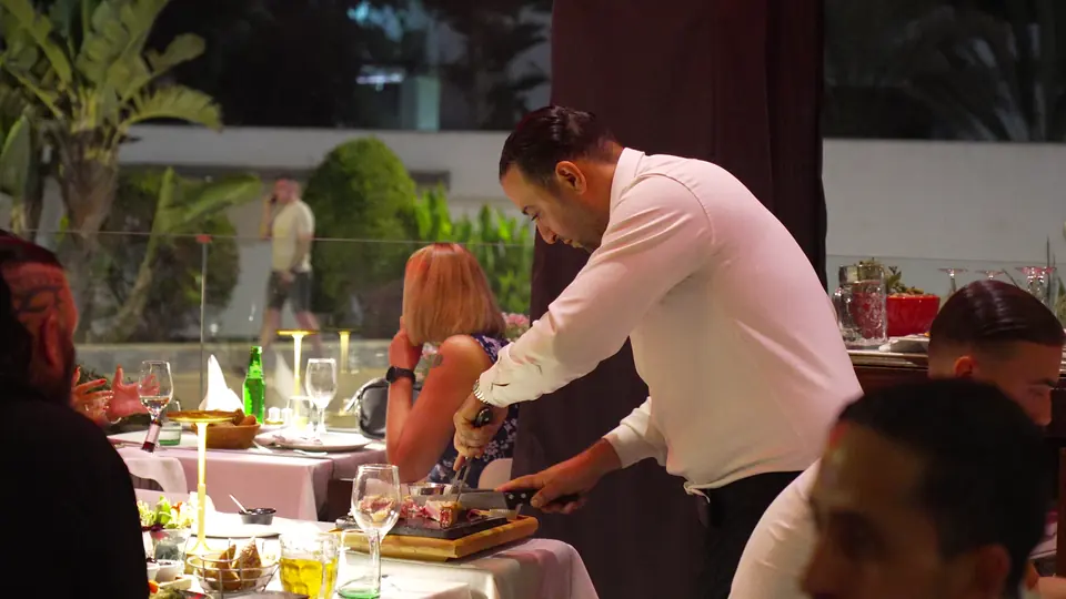 Un serveur découpe la viande à une table de la terrasse