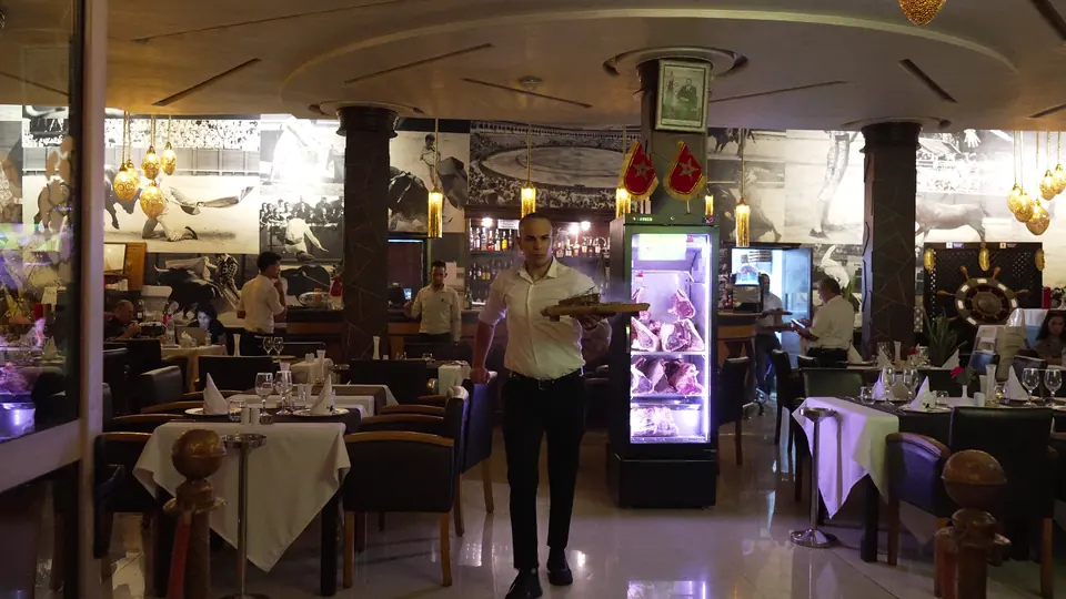 Un serveur traverse la salle avec un plateau ; la vitrine de bœuf éclairée au fond
