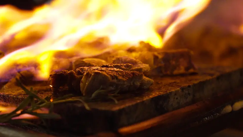 Gros plan sur une pièce de viande sur une pierre chaude, flammes et romarin