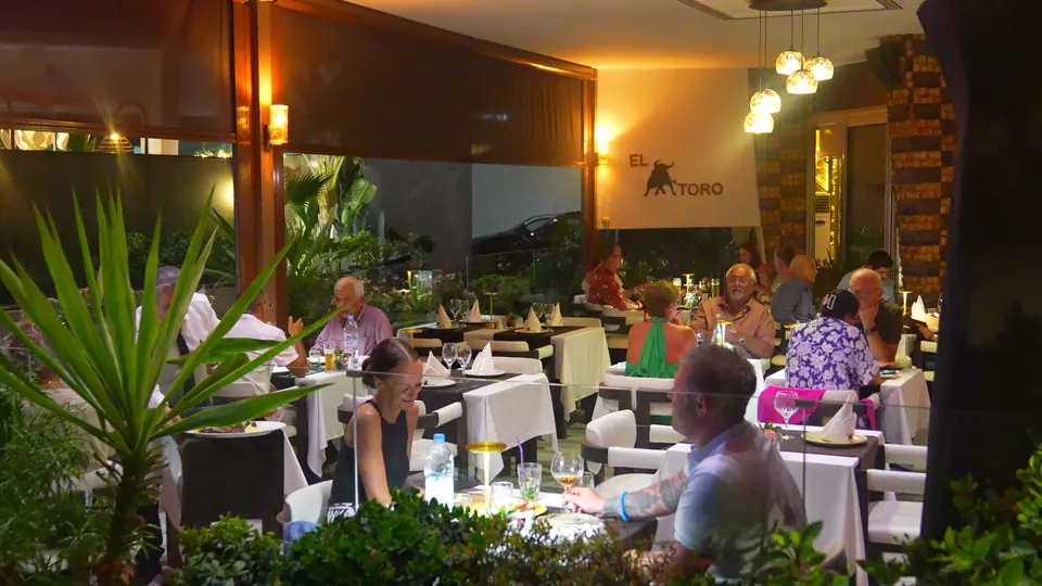 Soirée sur la terrasse : tables entre les palmiers, l’enseigne El Toro au fond